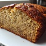 Close-up of a thick slice of moist sugar free banana bread showing its dense, speckled crumb and golden-brown crust.