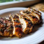 Close-up of perfectly cooked, sliced greek chicken breast seasoned with herbs on a white plate.