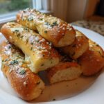 A stack of soft, golden brown garlic breadsticks topped with melted butter, minced garlic, and parsley.