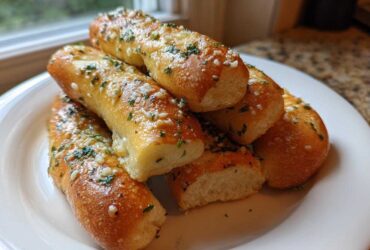 A stack of soft, golden brown garlic breadsticks topped with melted butter, minced garlic, and parsley.