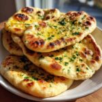 A stack of freshly baked, soft naan bread brushed with melted butter and topped with chopped parsley.