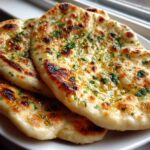 Close-up of three pieces of soft naan bread brushed with melted butter and sprinkled with fresh green herbs.