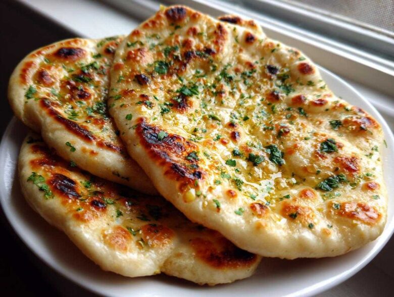 Close-up of three pieces of soft naan bread brushed with melted butter and sprinkled with fresh green herbs.