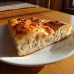Cross-section of a thick slice of baked sourdough discard pizza dough showing large air pockets and a cheesy top.