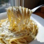 Close-up of spaghetti being lifted by a fork, coated generously in creamy homemade alfredo sauce and sprinkled with herbs.