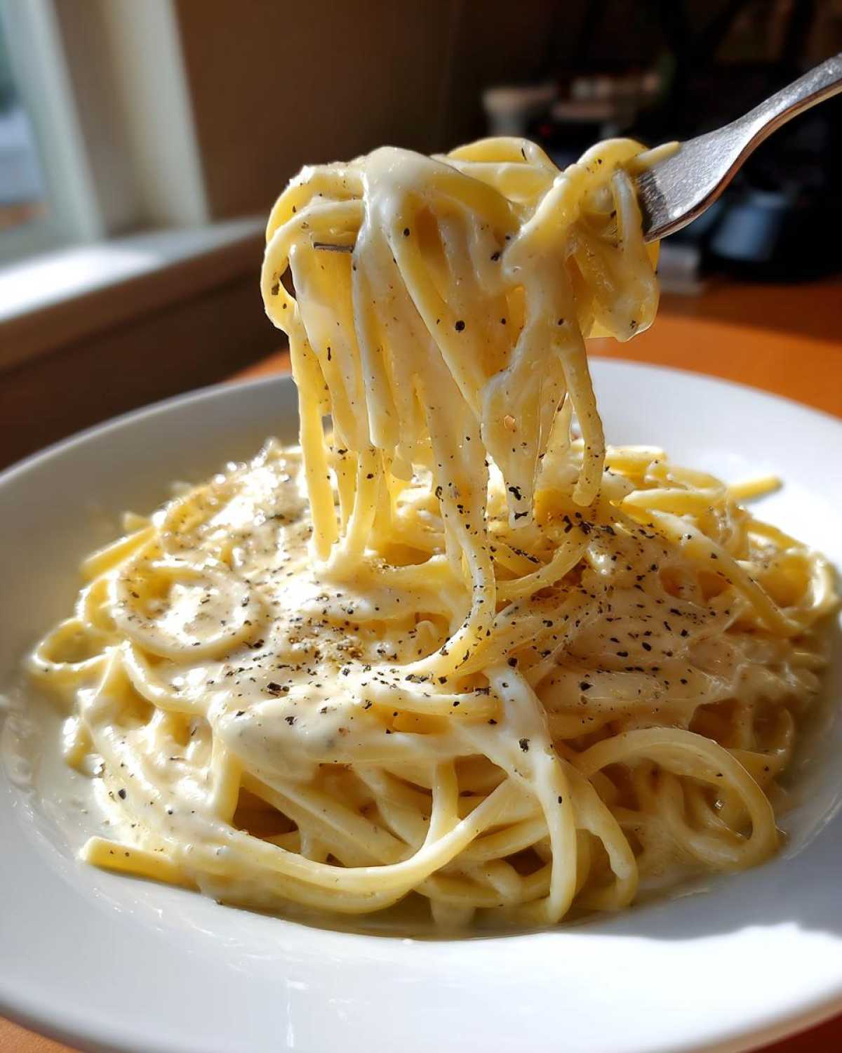 Close-up of spaghetti coated in rich homemade alfredo sauce being lifted by a fork, topped with black pepper.