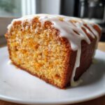 A moist slice of sweet potato pound cake topped with a thick, dripping white glaze, served on a white plate.
