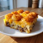 A close-up slice of tater tot breakfast casserole featuring crispy tots, melted cheese, and sausage layers.