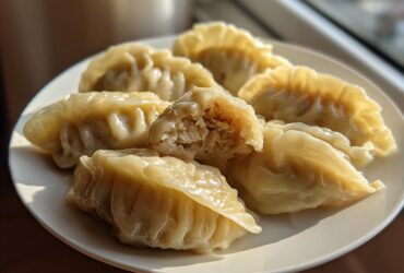 Close-up of several perfectly pleated Traditional Chinese Dumplings served on a white plate, one is broken open showing the filling.