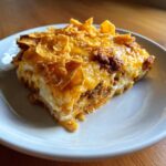 A close-up serving of Ultimate Dorito Casserole topped with melted cheese and crunchy chips.
