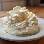 A perfect swirl of light yellow vanilla buttercream frosting piped onto a small white saucer.