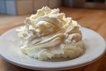 A perfect swirl of light yellow vanilla buttercream frosting piped onto a small white saucer.