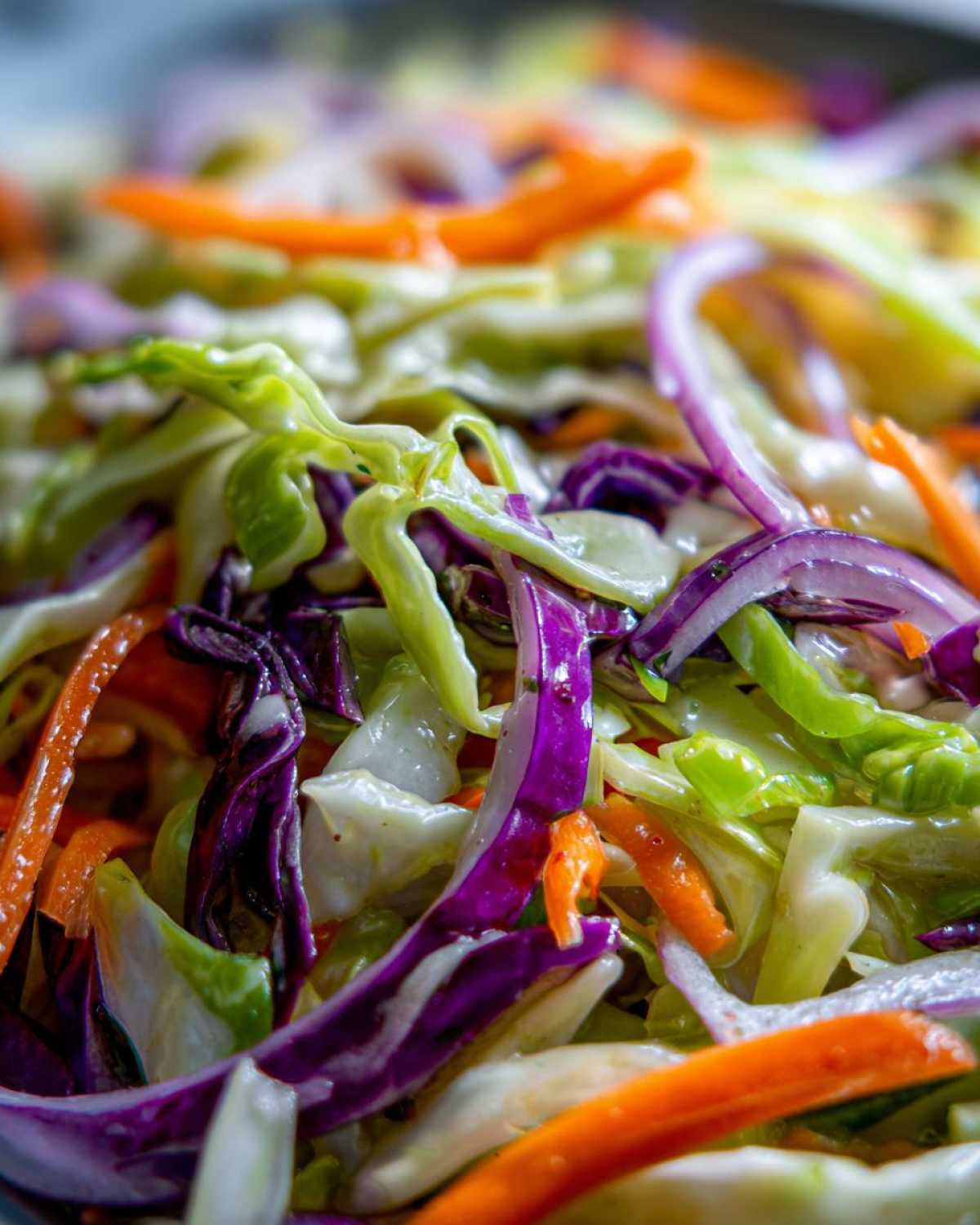 Extreme close-up of shredded green and purple cabbage, carrots, and red onion in a fresh cabbage salad.