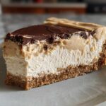 A thick slice of creamy peanut butter pie showing graham cracker crust, light filling, peanut butter layer, and chocolate ganache topping.