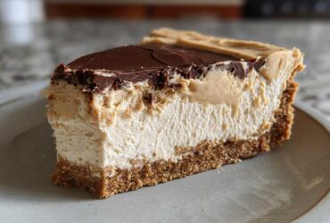 A thick slice of creamy peanut butter pie showing graham cracker crust, light filling, peanut butter layer, and chocolate ganache topping.