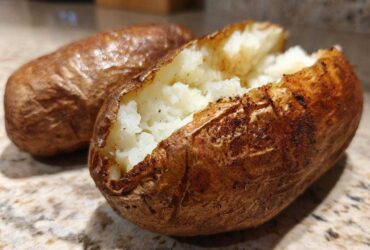 Close-up of a perfectly cooked air fryer baked potato, split open to show the fluffy white interior.