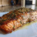 A close-up of a beautifully cooked fillet of air fryer salmon, glistening with butter and topped with minced garlic and herbs.