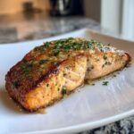 A close-up of a beautifully browned fillet of air fryer salmon topped with melted butter and fresh parsley.