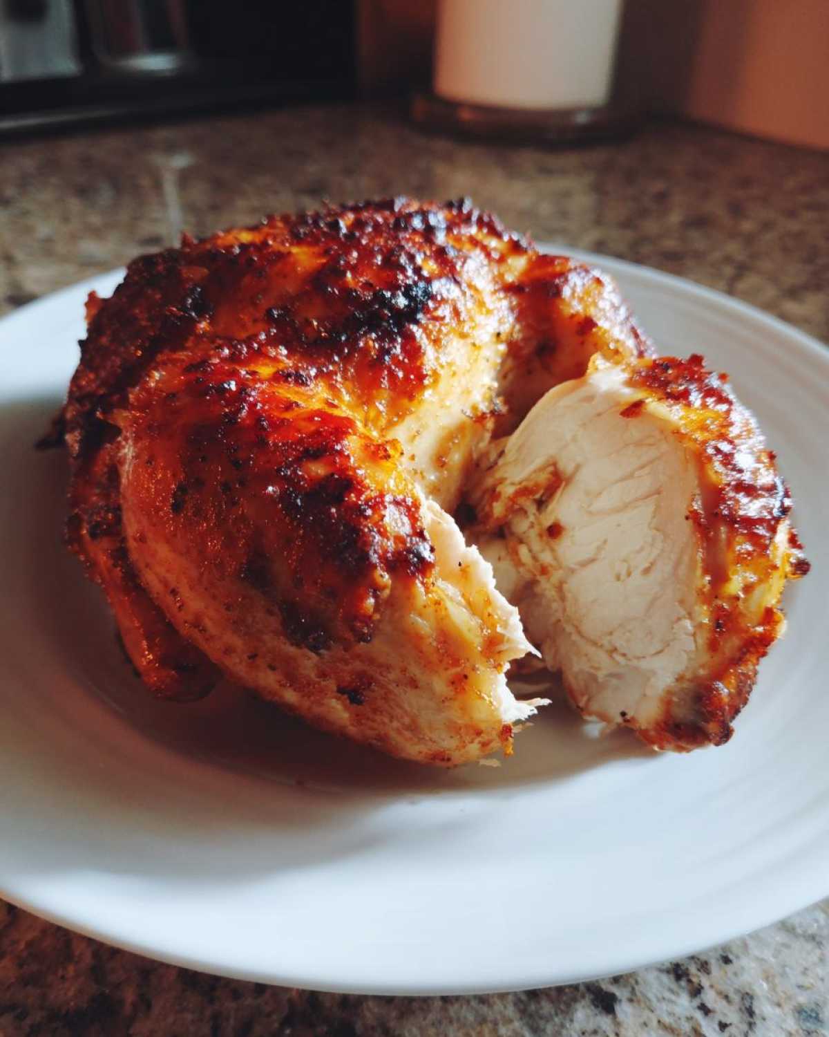 A piece of juicy air fryer whole chicken with perfectly browned, crispy skin, resting on a white plate.