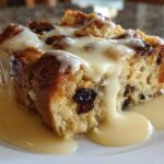 A close-up of a slice of amazing bread pudding topped with vanilla sauce and raisins.