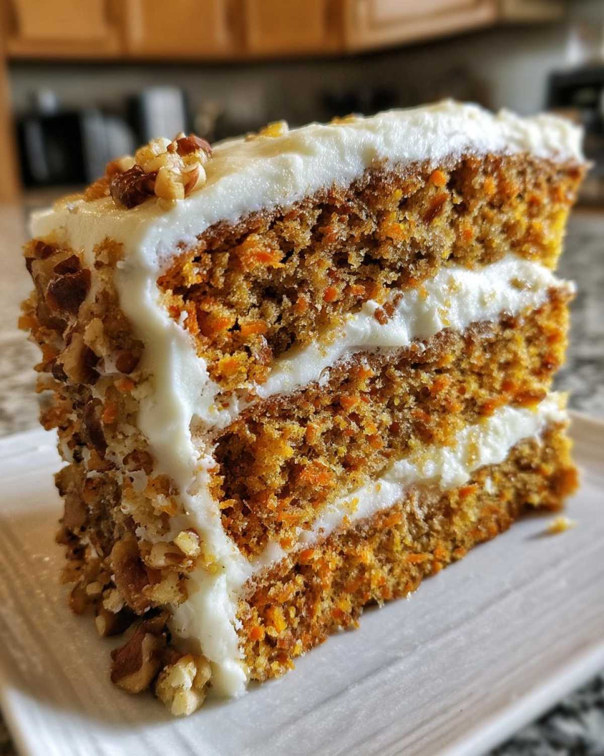 Close-up of a thick slice of amazing carrot cake recipe with two layers, cream cheese frosting, and chopped pecans.