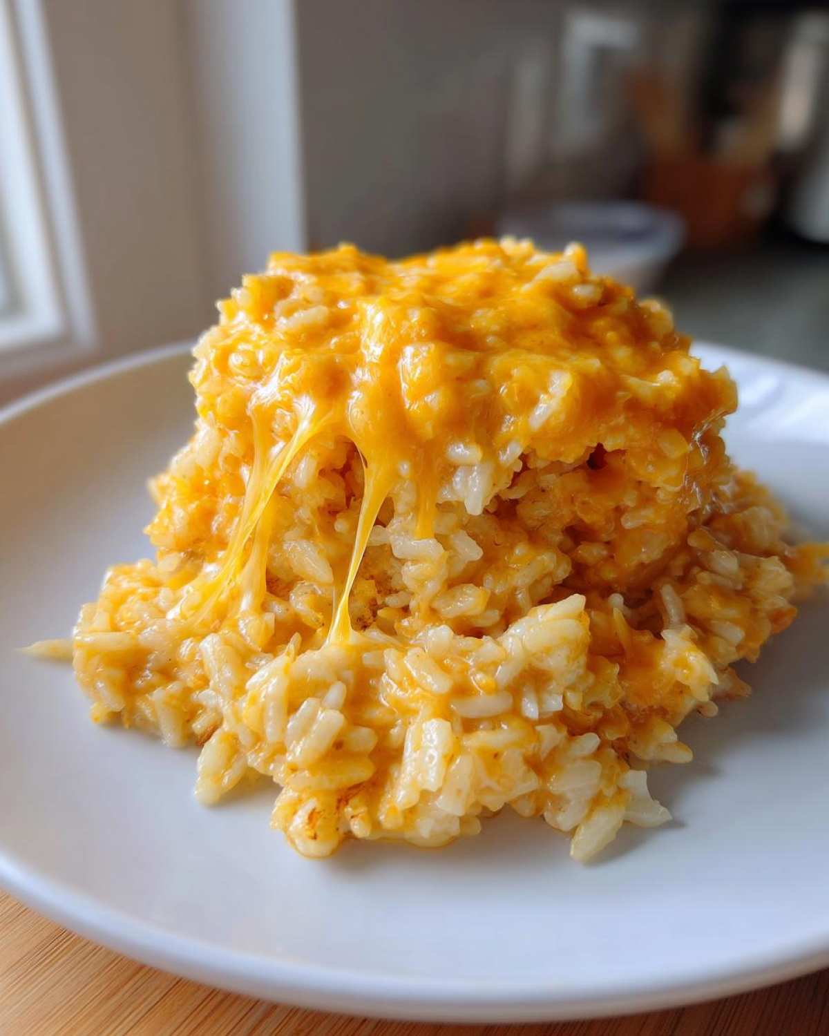 A serving of creamy, bright orange cheesy rice on a white plate with melted cheddar cheese stretching down.