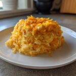 A molded serving of creamy, orange cheesy rice topped with shredded cheddar cheese on a white plate.