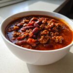 Close-up of a rich, thick bowl of amazing crockpot chili featuring ground meat and kidney beans.