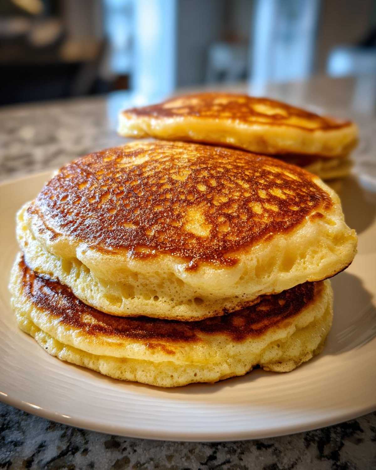 Close-up of a stack of three perfectly cooked, fluffy pancakes with golden brown tops.