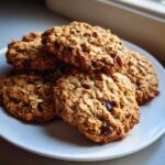 A stack of freshly baked, chewy oatmeal cookie with visible chocolate chips on a white plate.