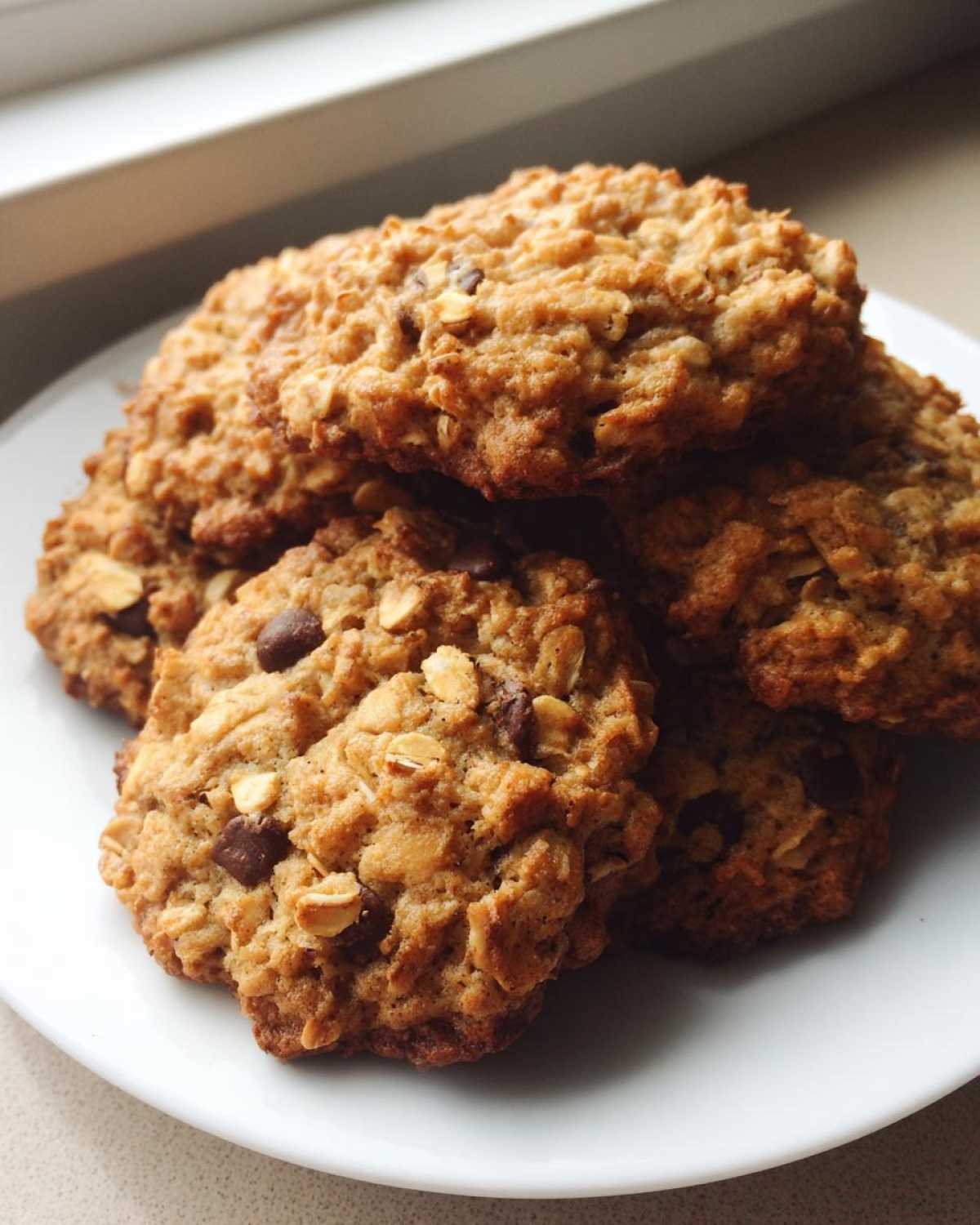 A close-up of several freshly baked oatmeal cookie treats stacked on a white plate.