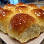 Close-up of a pan of freshly baked, soft dinner rolls with a shiny, golden-brown butter glaze.