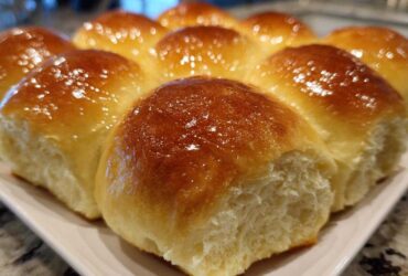 Close-up of a pan of freshly baked, soft dinner rolls with a shiny, golden-brown butter glaze.