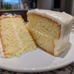 Two slices of moist vanilla cake recipe covered in thick white buttercream frosting on a white plate.