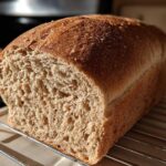 A close-up of a freshly baked whole wheat bread loaf, showing the soft, open crumb structure, resting on a cooling rack.