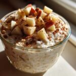 A glass jar filled with creamy apple cinnamon overnight oats, topped with diced apples and a dusting of cinnamon.