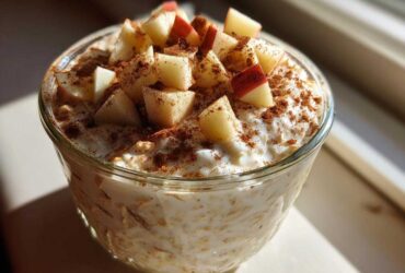 A glass jar filled with creamy apple cinnamon overnight oats, topped with diced apples and a dusting of cinnamon.