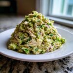 A generous mound of creamy avocado chicken salad featuring shredded chicken and red onion chunks.