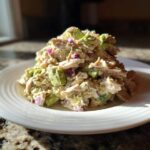 A serving of creamy avocado chicken salad mixed with chunks of avocado and red onion on a white plate.