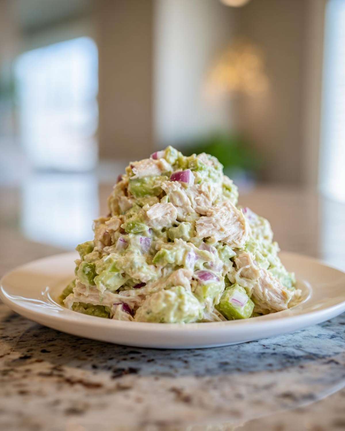 A generous scoop of creamy avocado chicken salad mixed with red onion chunks, served on a white plate.
