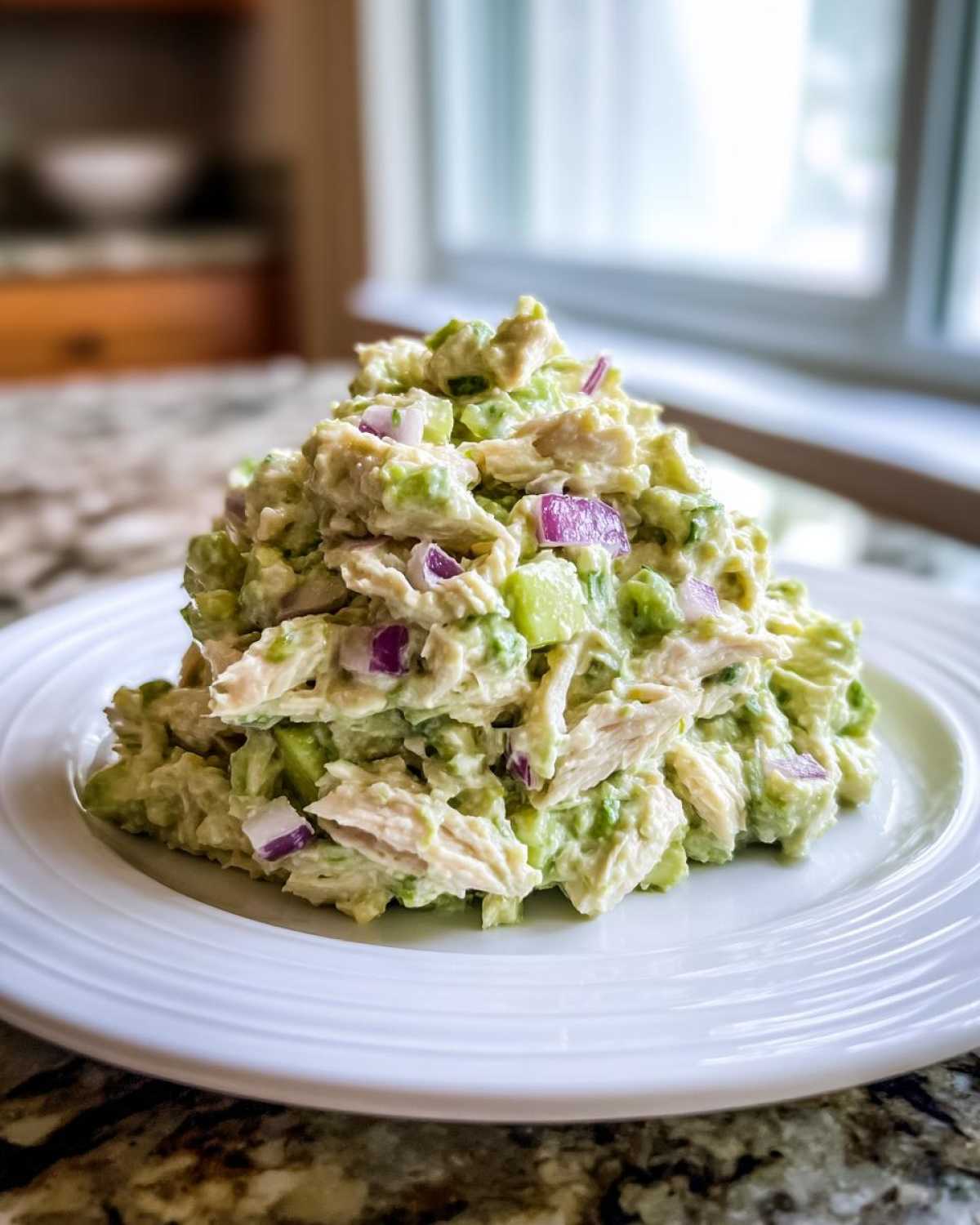 A generous scoop of creamy avocado chicken salad mixed with red onion and celery on a white plate.