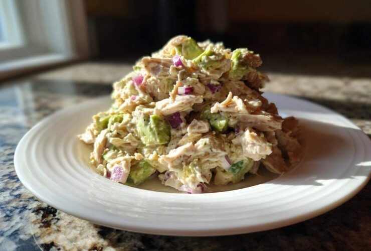 A serving of creamy avocado chicken salad mixed with chunks of avocado and red onion on a white plate.