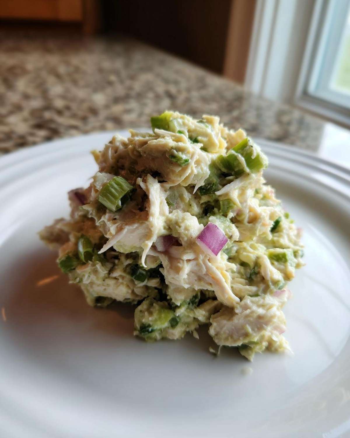 A scoop of creamy avocado chicken salad mixed with green celery and purple onion served on a white plate.