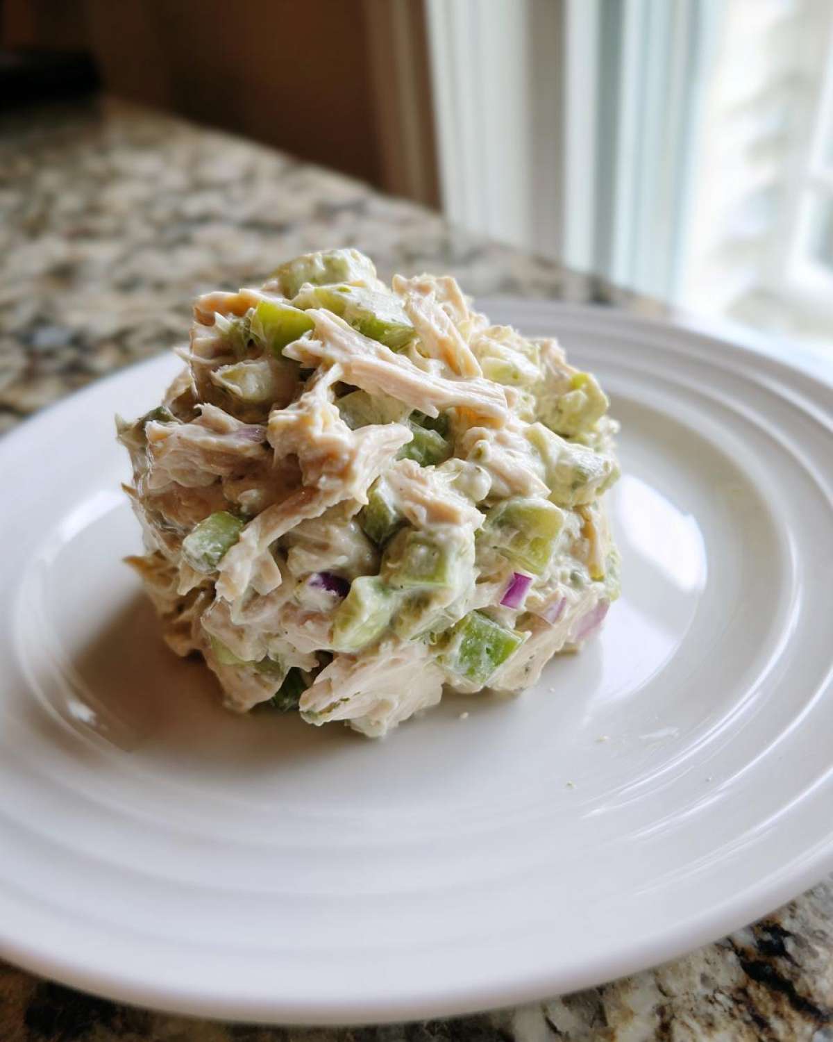 A mound of creamy avocado chicken salad with celery and red onion served on a white plate.