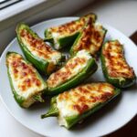 Six baked jalapeño poppers stuffed with creamy cheese filling and topped with browned, melted cheese.