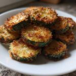 A serving of crispy, golden brown baked parmesan zucchini slices piled on a white plate.