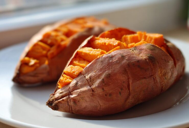 Two perfectly baked sweet potatoes, scored and fluffed, sitting on a white plate.
