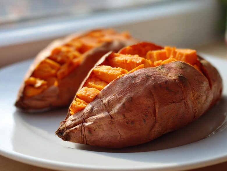 Two perfectly baked sweet potatoes, scored and fluffed, sitting on a white plate.