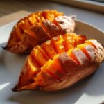 Two perfectly baked sweet potatoes, sliced accordion-style, showing fluffy orange flesh.