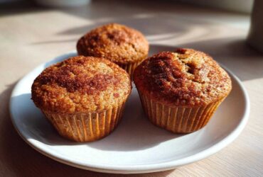 Three freshly baked banana protein muffins dusted with cinnamon sugar sitting on a white plate.